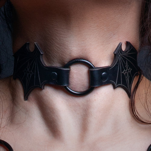 Black leather bat wing choker with etched gothic pattern and black O-ring, worn on the neck