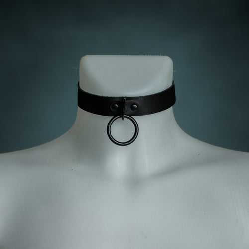Black leather O-ring choker with black hardware on a white mannequin, front view, by Wandering Chaos